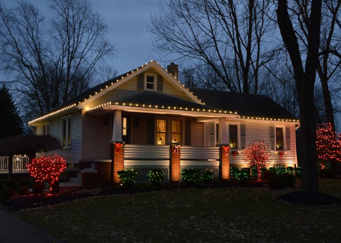 Holiday lighting at a small white and brick ranch house